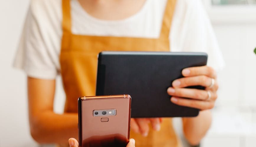 crop worker with tablet against partner with smartphone in cafe